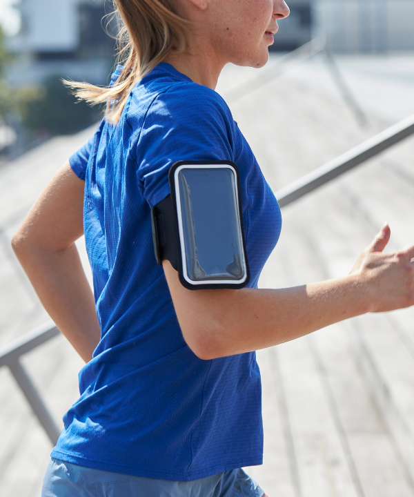 Una donna che corre all'aperto, con un bracciale sportivo magnetico Shapeheart con pochette staccabile, fissato sul suo braccio.