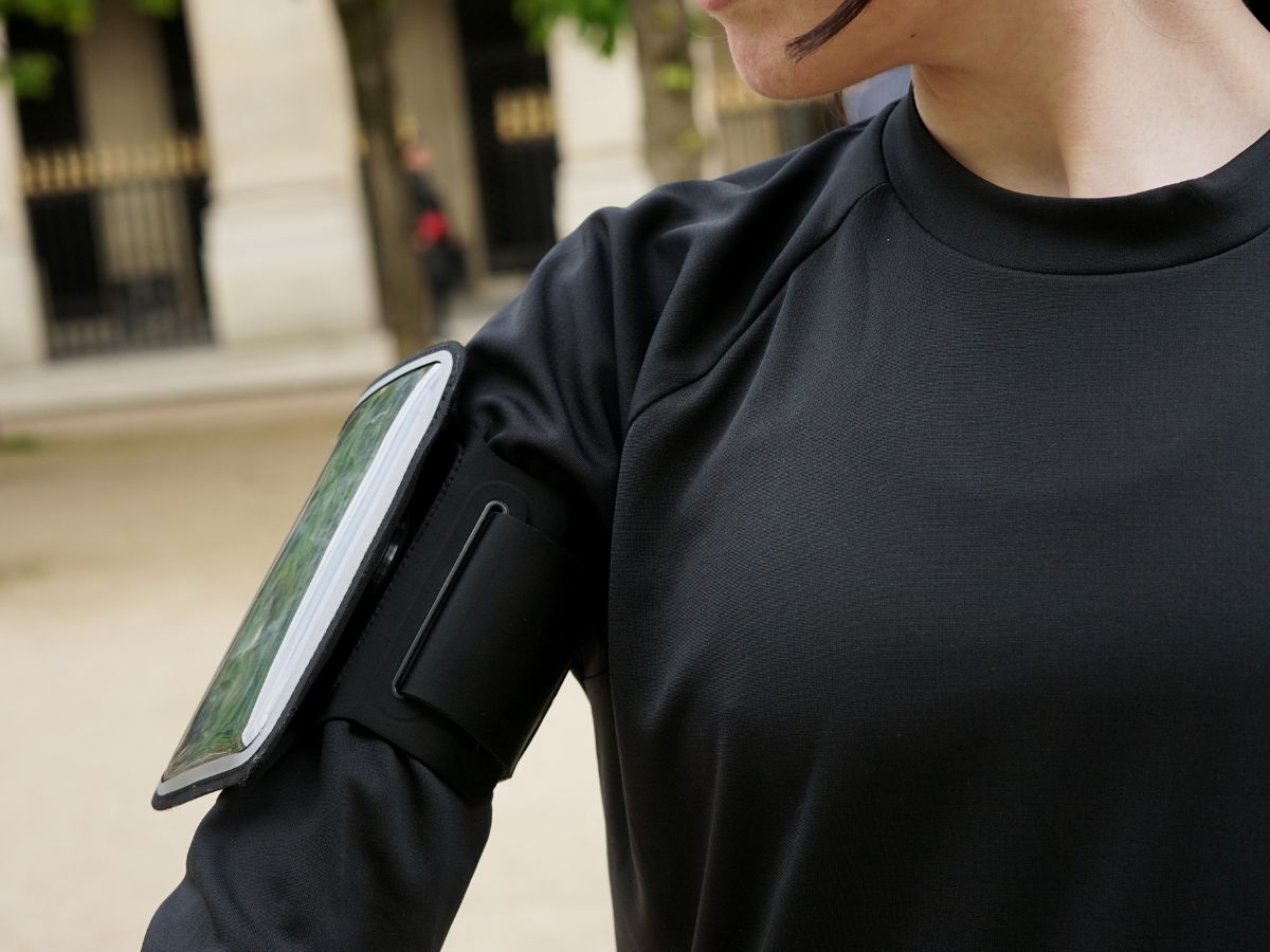 Jogger con giacca impermeabile che corre sotto la pioggia con un bracciale impermeabile visibile sul braccio, che illustra la protezione degli oggetti elettronici durante la corsa.