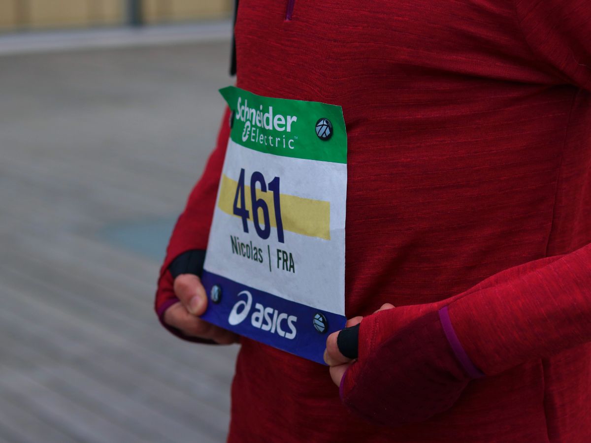 Atleta alla partenza di una competizione che indossa un pettorale tenuto da magneti su una maglia tecnica, a illustrare la preparazione ottimale per una gara ufficiale.