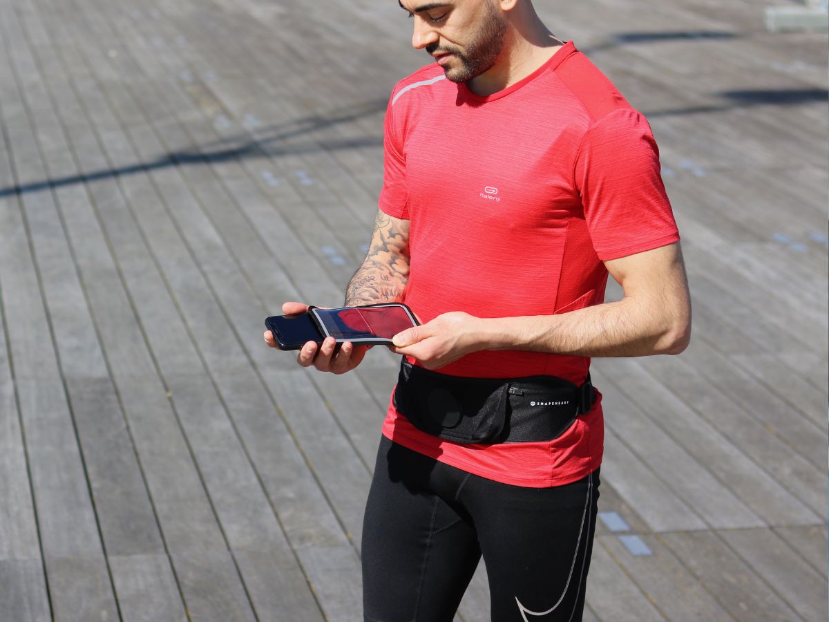 Jogger con giacca impermeabile che corre sotto la pioggia con un bracciale impermeabile visibile sul braccio, che illustra la protezione dei dispositivi elettronici durante la corsa.