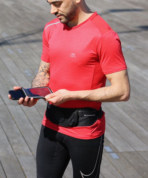 Jogger con giacca impermeabile che corre sotto la pioggia con un bracciale impermeabile visibile sul braccio, a illustrare la protezione dei dispositivi elettronici durante la corsa.