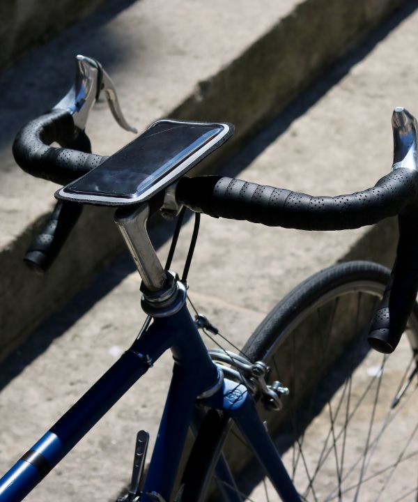 Supporto smartphone magnetico fissato sul manubrio di una bici da strada, con un'app GPS attiva sullo schermo.