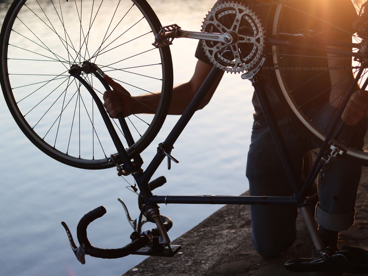 Ciclista che ferma la bici per riparare una foratura, con una mini-pompa e una camera d'aria ai suoi piedi.