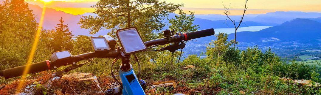 Ciclista che consulta uno smartphone e un GPS bici fianco a fianco prima di un'uscita, illustrando la scelta tra due opzioni di navigazione.