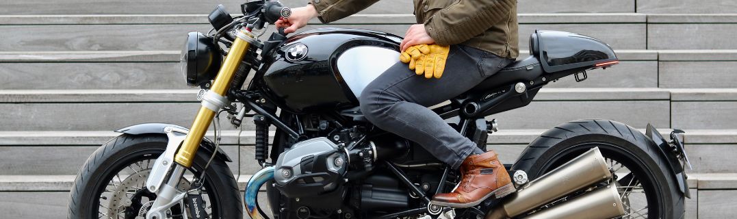 Giovane motociclista in tenuta, felice di iniziare con la sua prima moto, pronto ad equipaggiarsi per guidare in sicurezza.