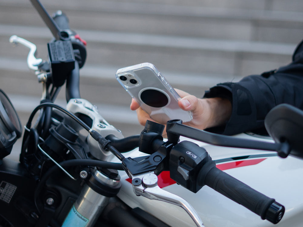 Motociclista che fissa il suo smartphone sul supporto telefono moto pro con piastra montato sul manubrio della sua moto. Il supporto magnetico garantisce un fissaggio sicuro e rapido, ideale per la navigazione e l'utilizzo del telefono in tutta sicurezza su strada.